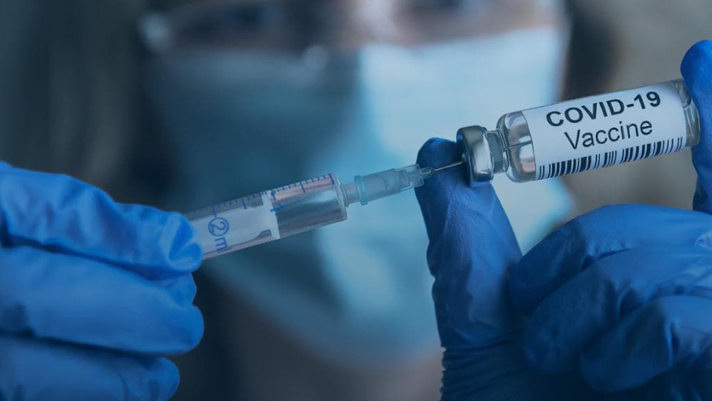A gloved hand drawing vaccine from a vial with a syringe