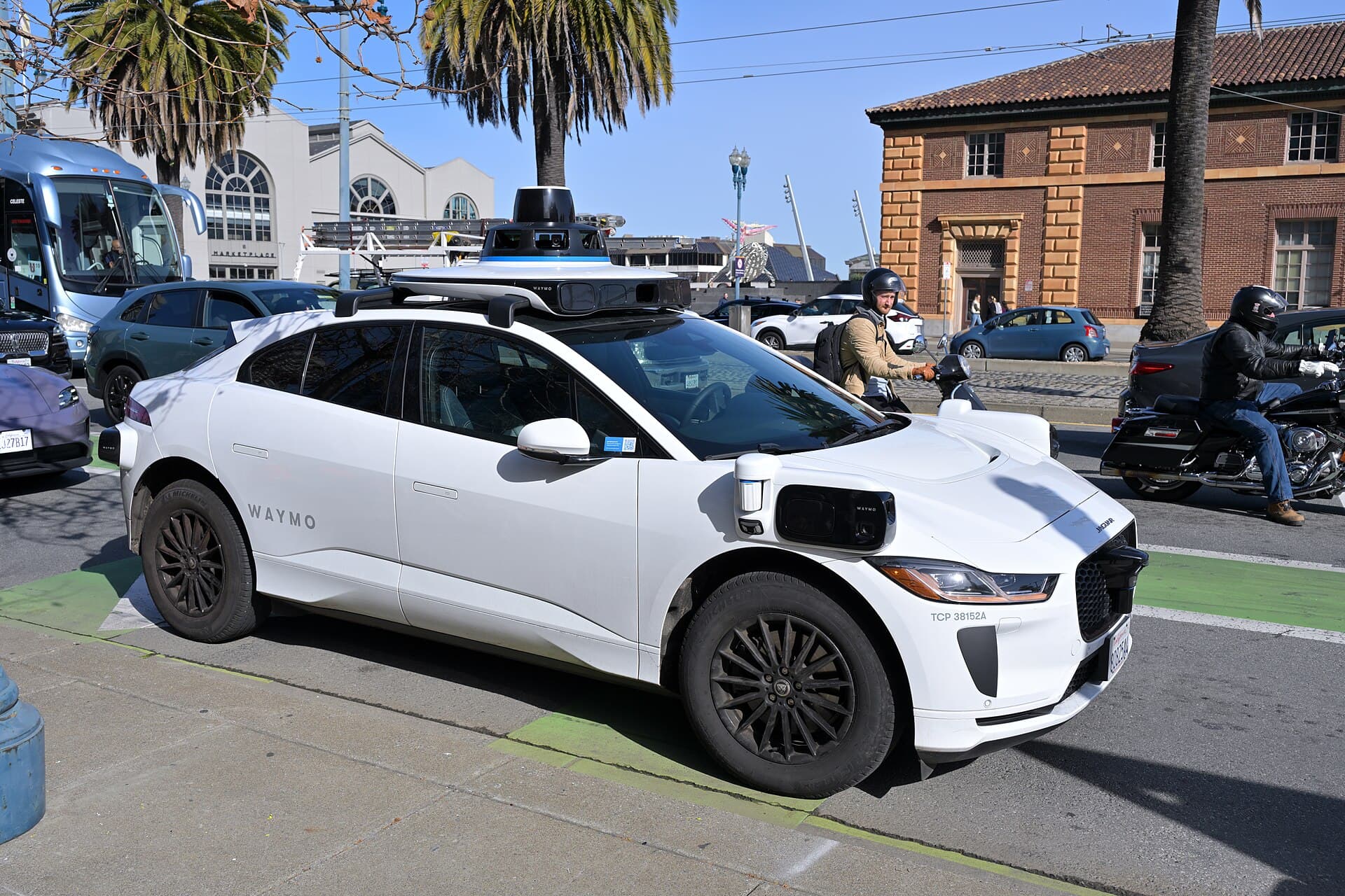 A white Waymo Jaguar I-Pace robotaxi with sensors on its roof driving in San Francisco